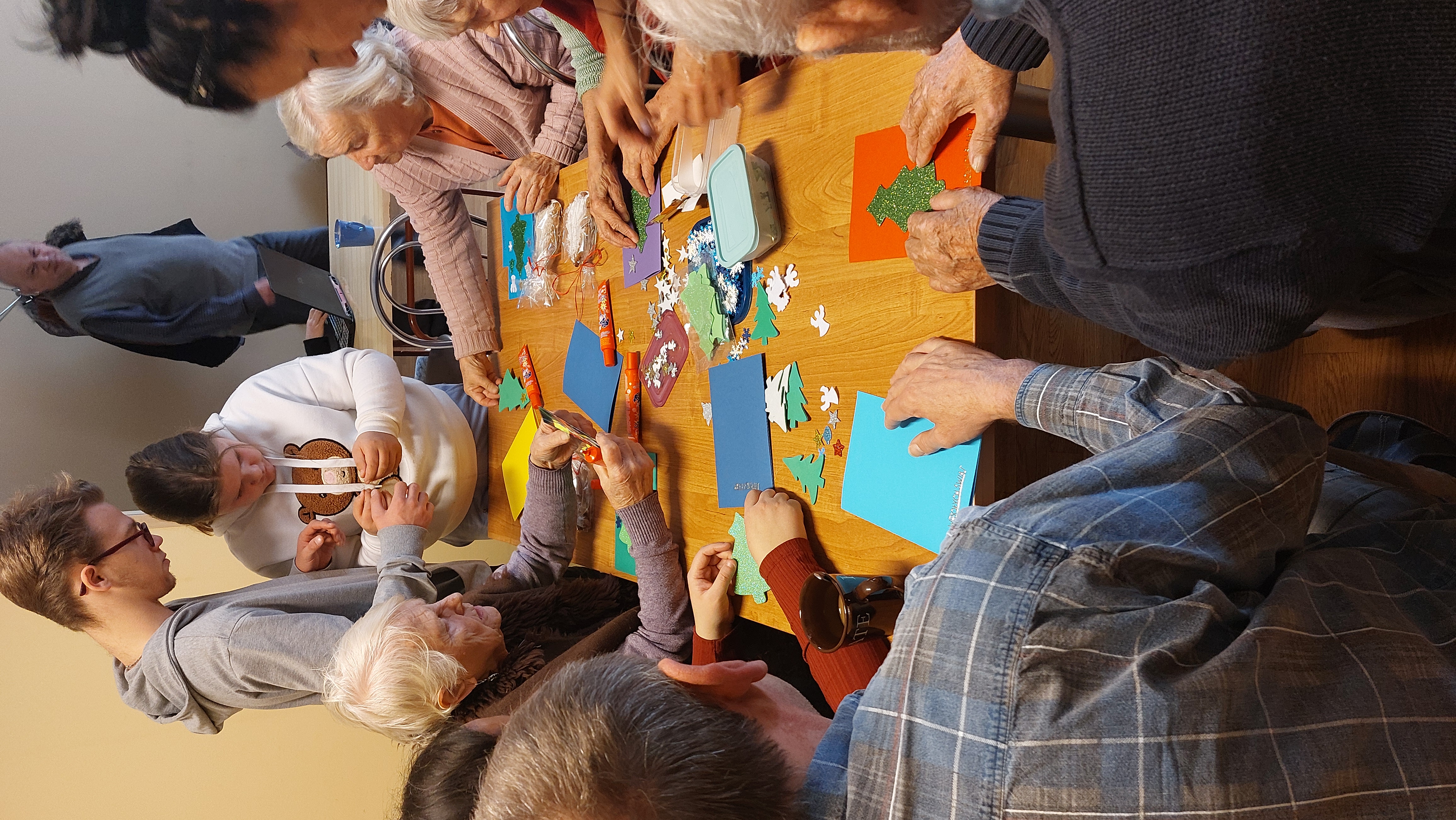 Seniorzy przy stole, wykonują ozdoby z kolorowego papieru