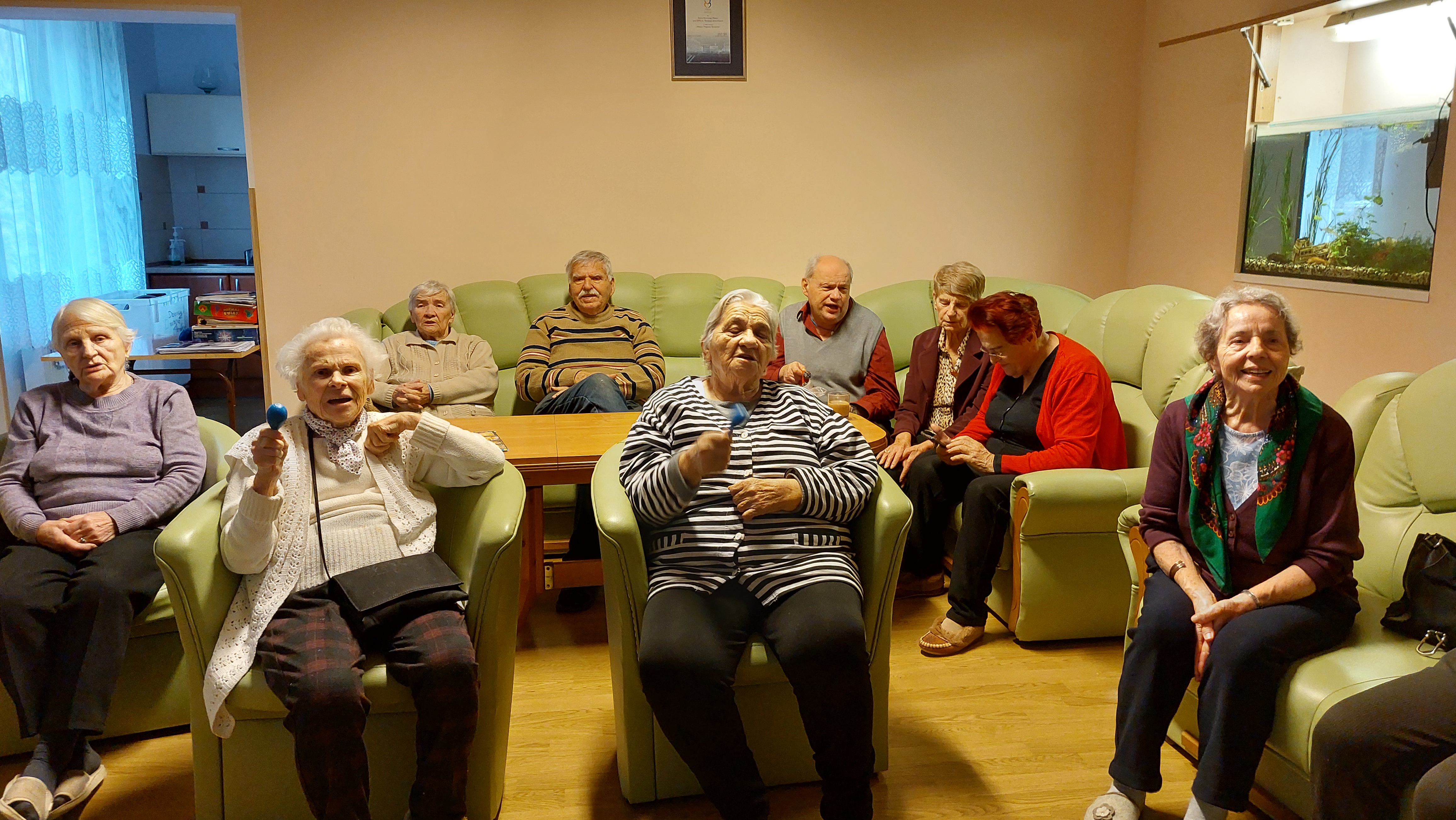 Seniorzy siedzący na sofach słuchając z zaciekawieniem młodzieży