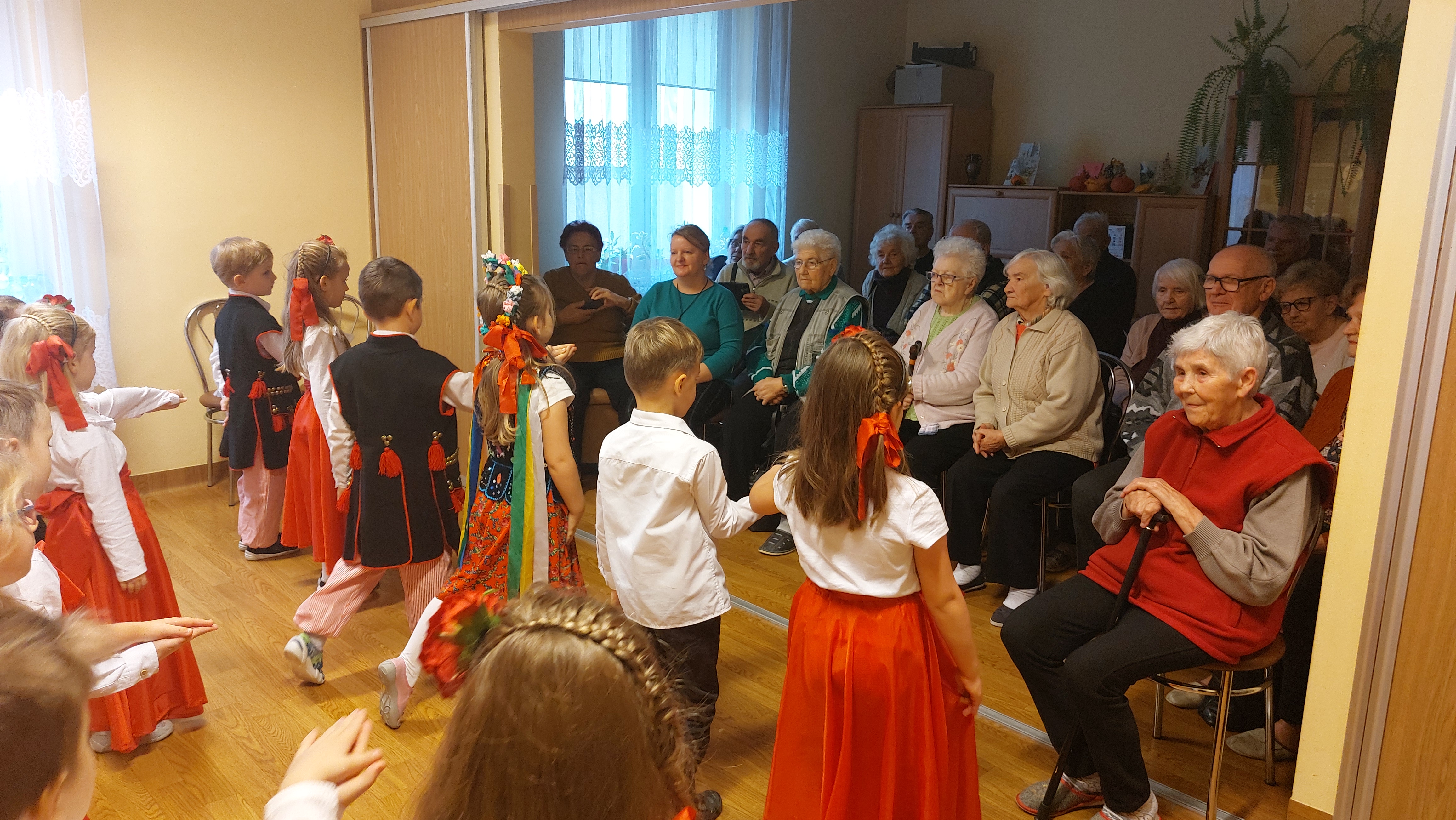Dzieci tańczą taniec ludowy, seniorzy przyglądają się z uwagą