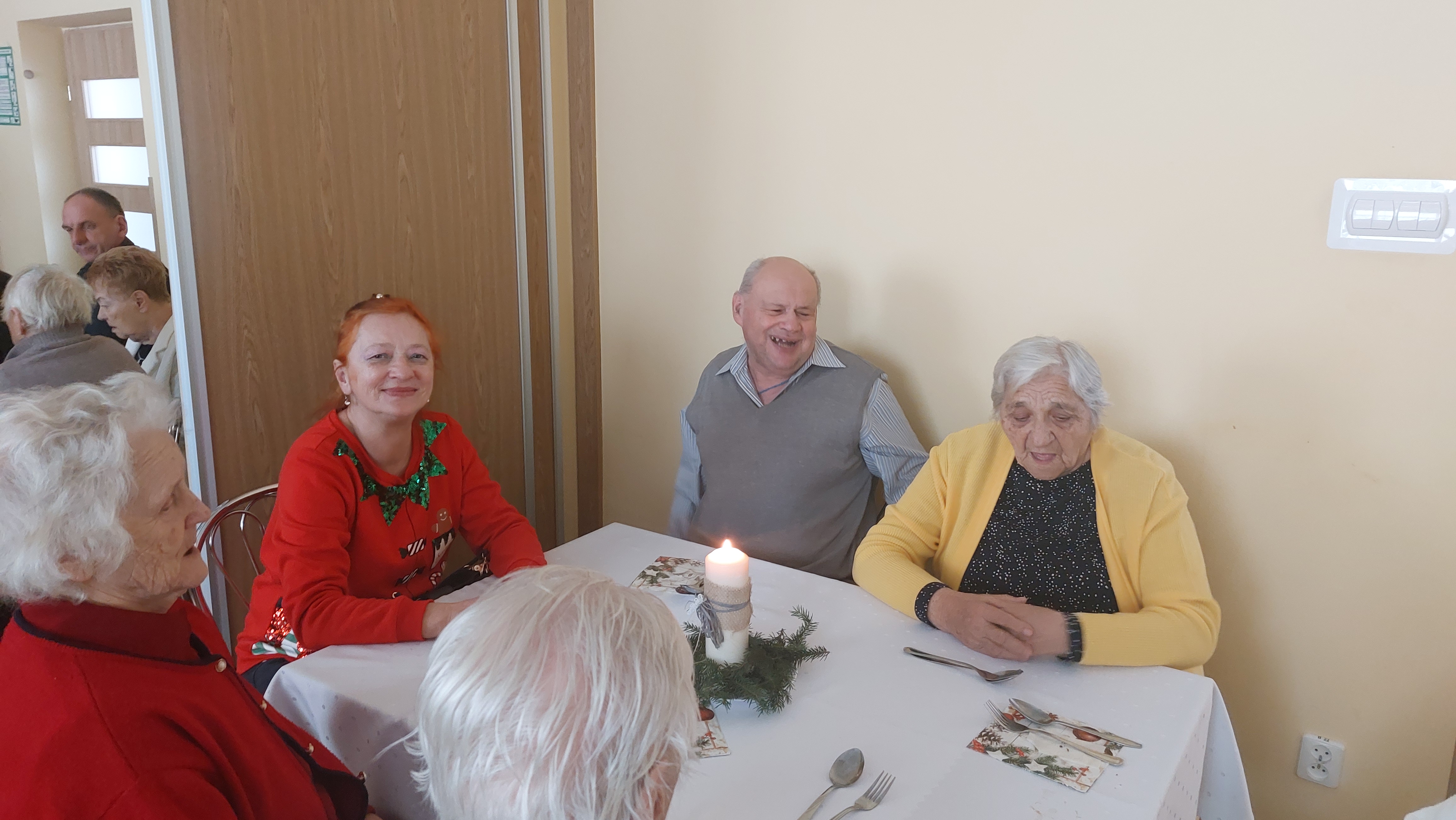 Seniorzy siedzą przy stole, na którym stoi zapalona świeczka