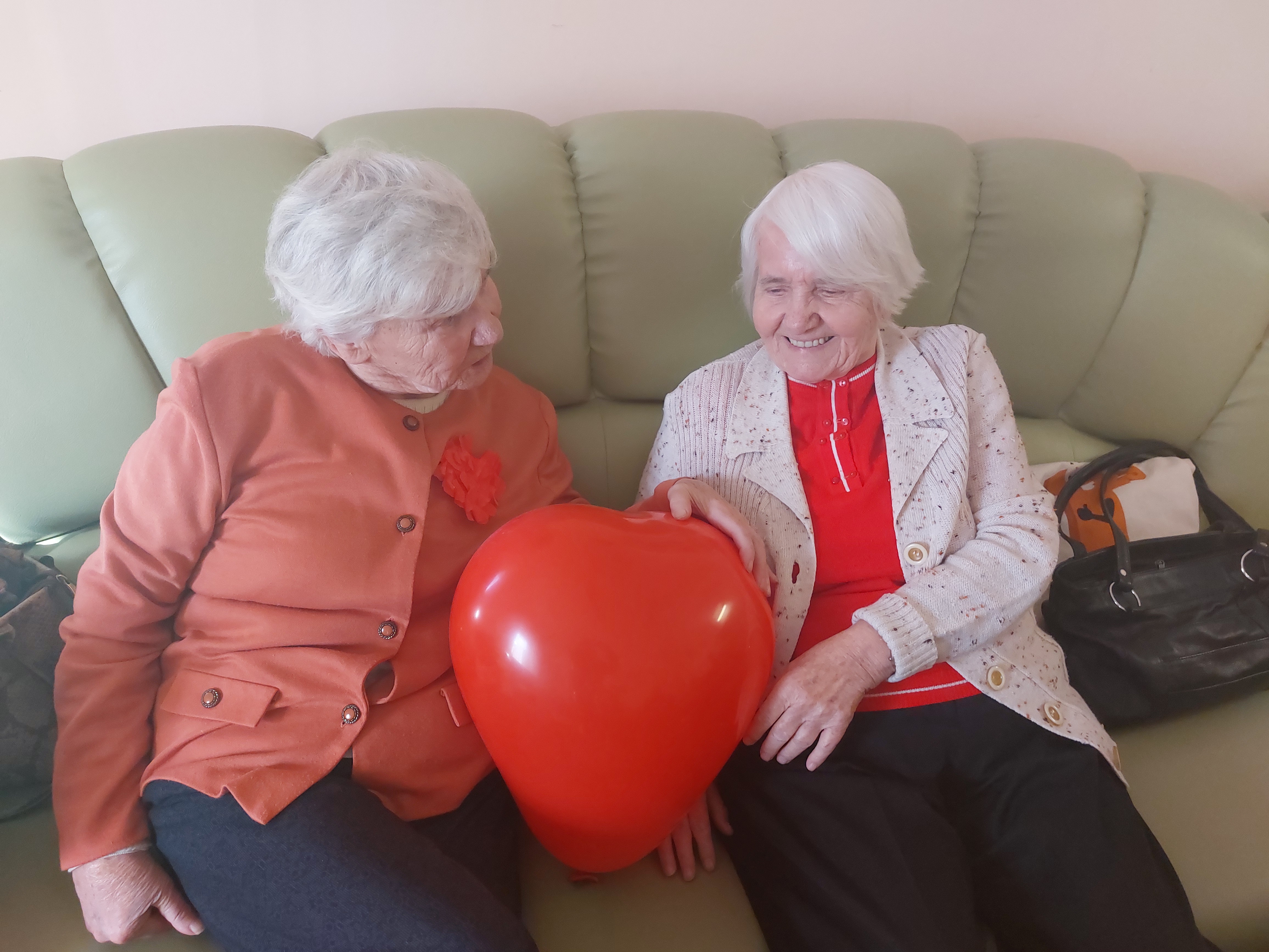 Dwie Seniorki siedzą na kanapie z balonem w kształcie serca