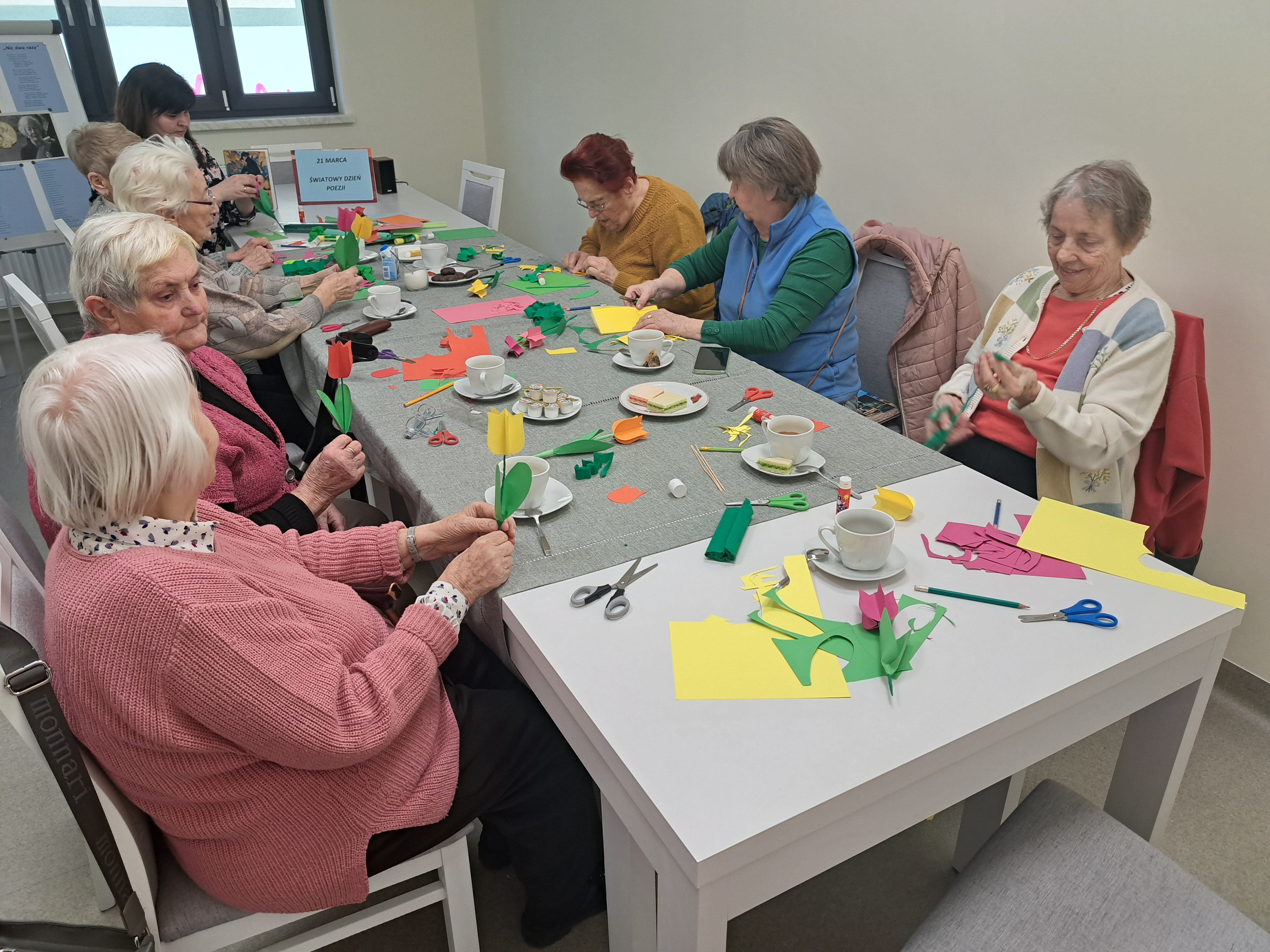Seniorki siedzą przy stole, przygotowują tulipany z papieru kolorowego