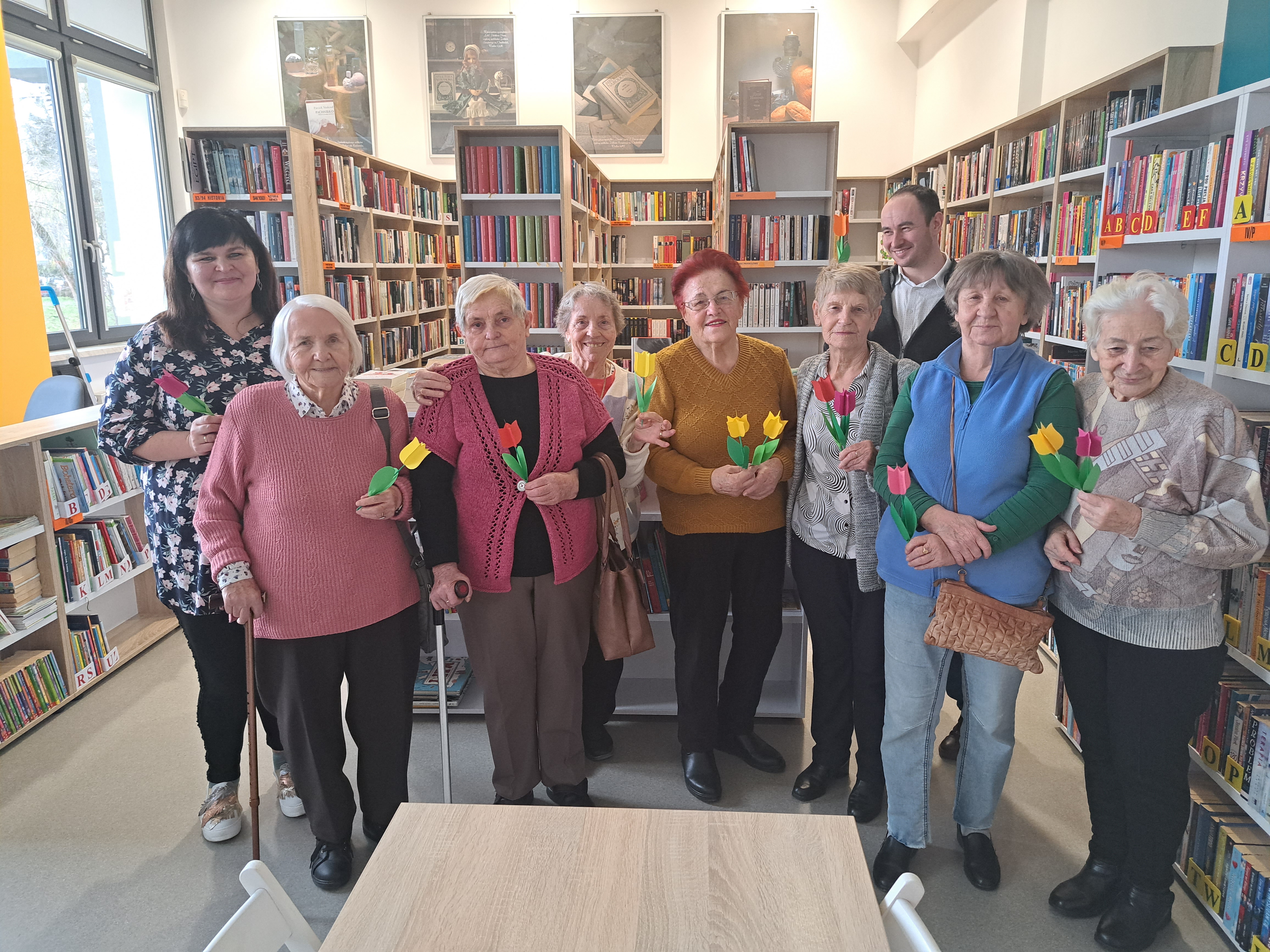Grupa Seniorek pozuje do zdjęcia z Panem Grzegorzem oraz Panią pracującą w bibliotece