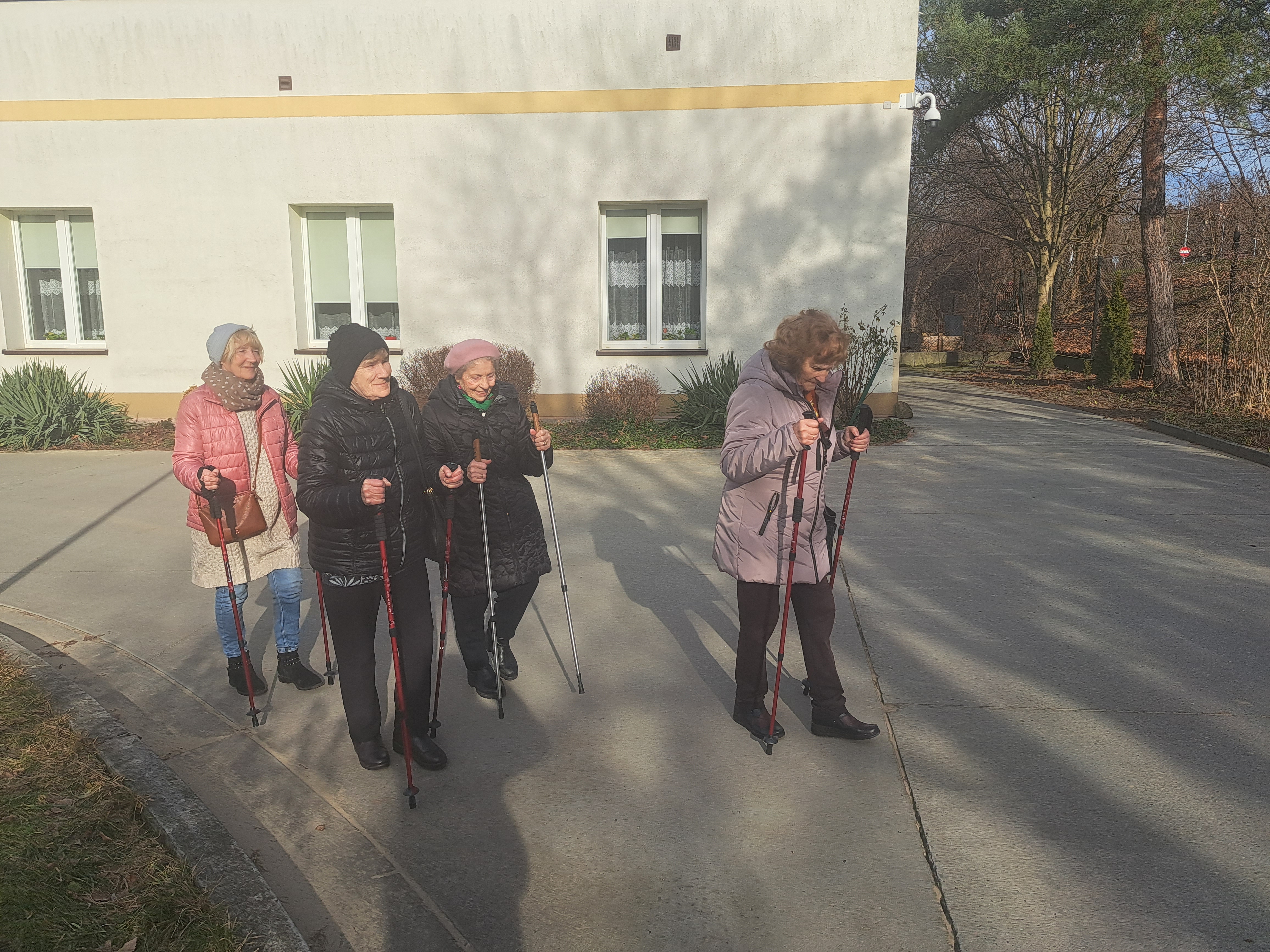 Seniorki spacerują przed domem z kijkami do nordic walking