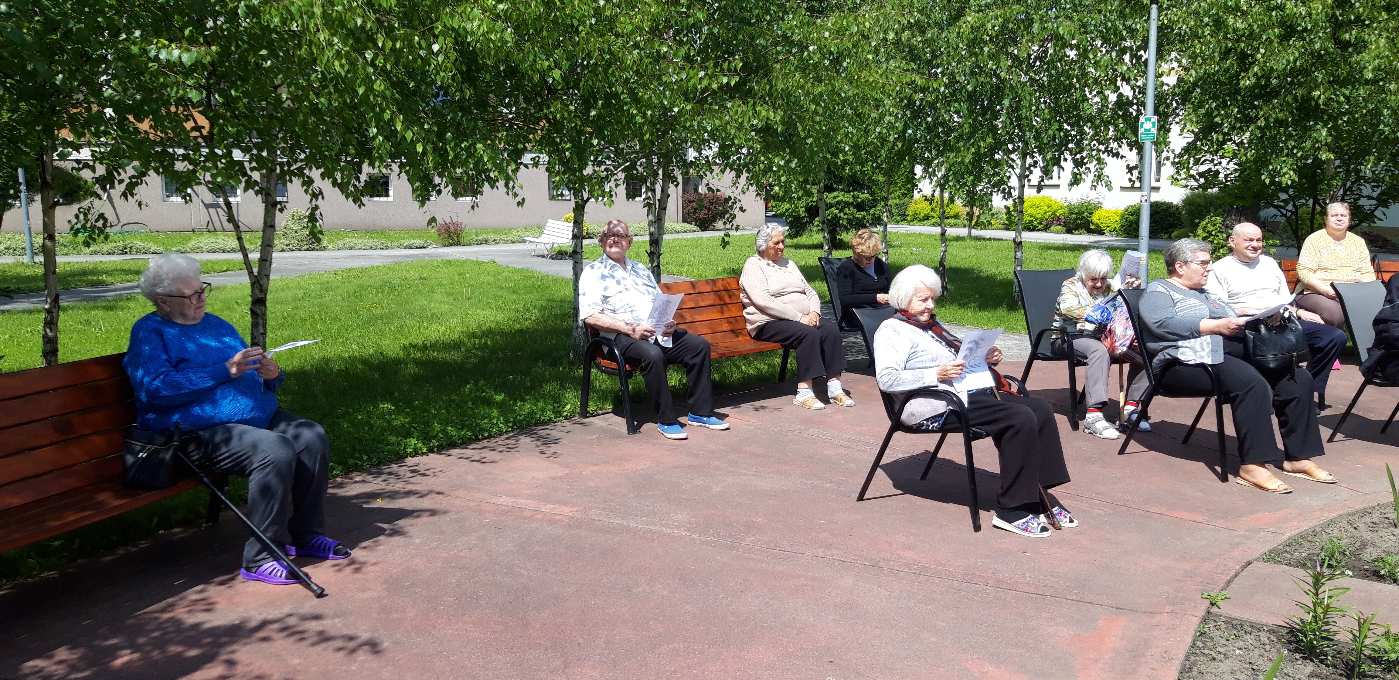 Seniorzy siedzą w odległosci od siebie w ogrodzie
