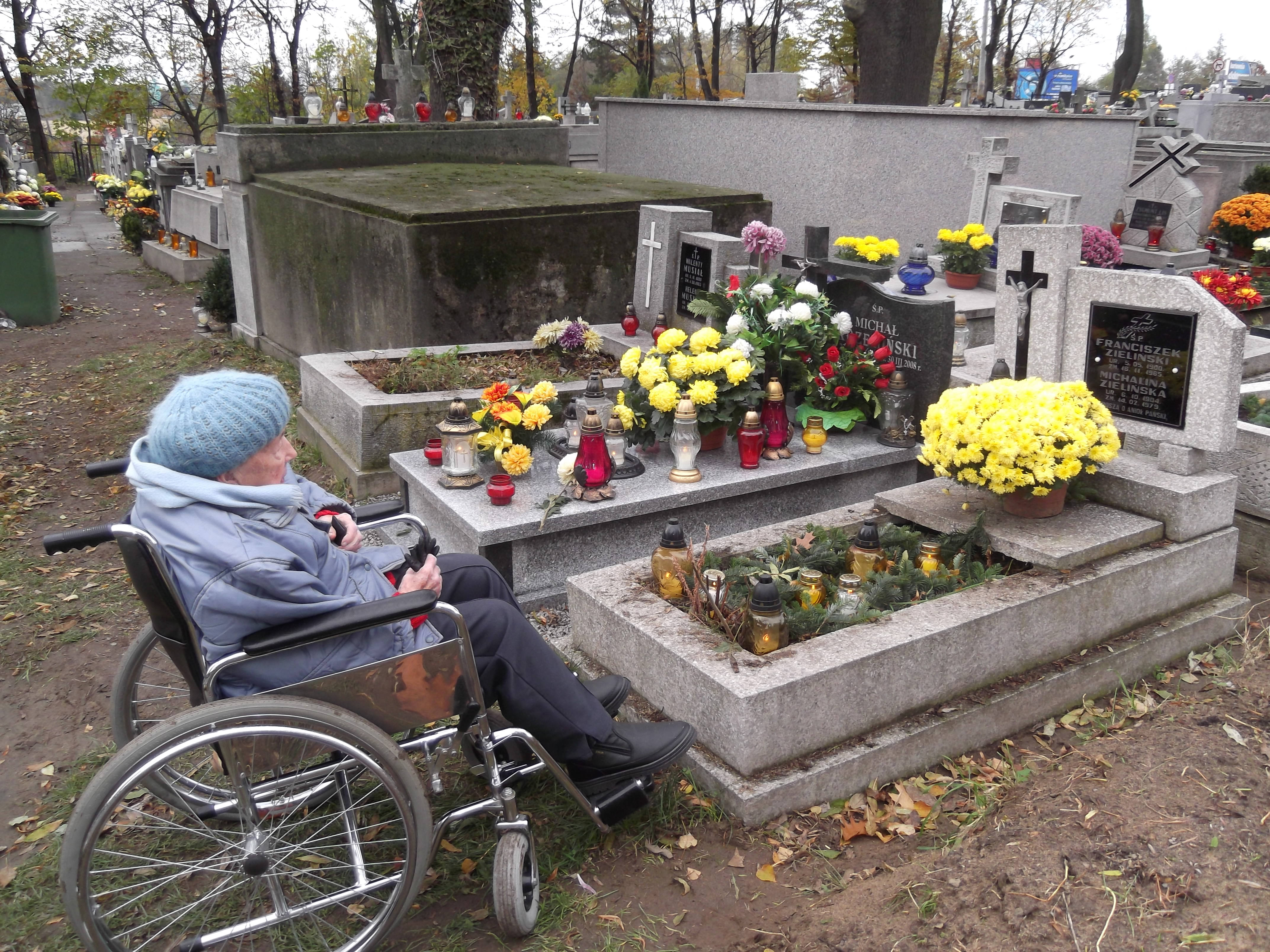 Seniorka na wózku siedzi przed grobem na cmentarzu