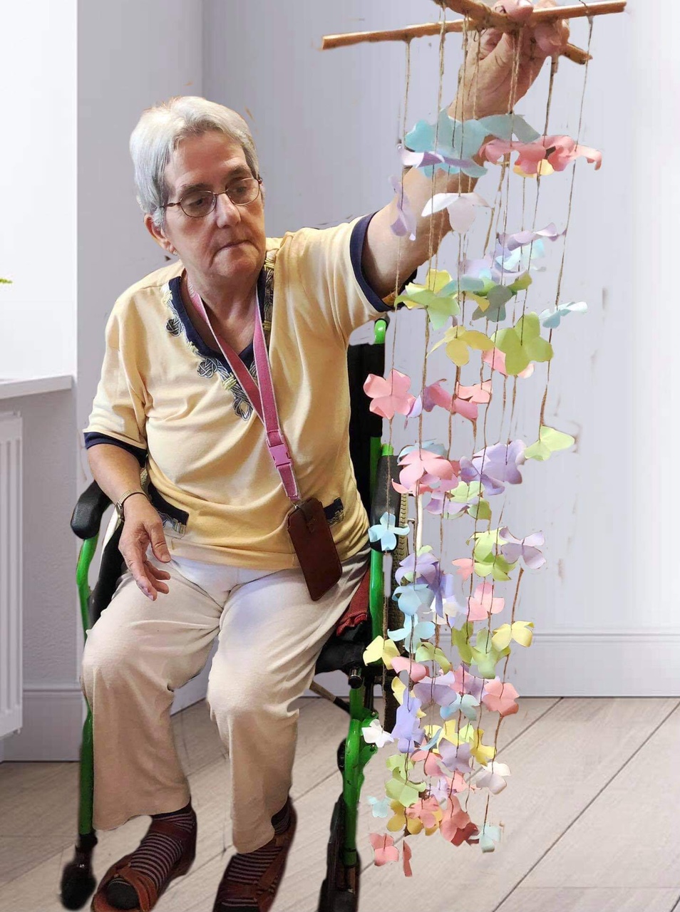 Seniorka trzyma wiszącą ozdobę z papierowych kwiatów