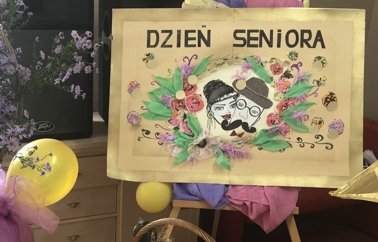 Ozdobna, własnoręcznie wykonana tablica z napisem Dzień Seniora i dwoma narysowanymi twarzami Seniorów