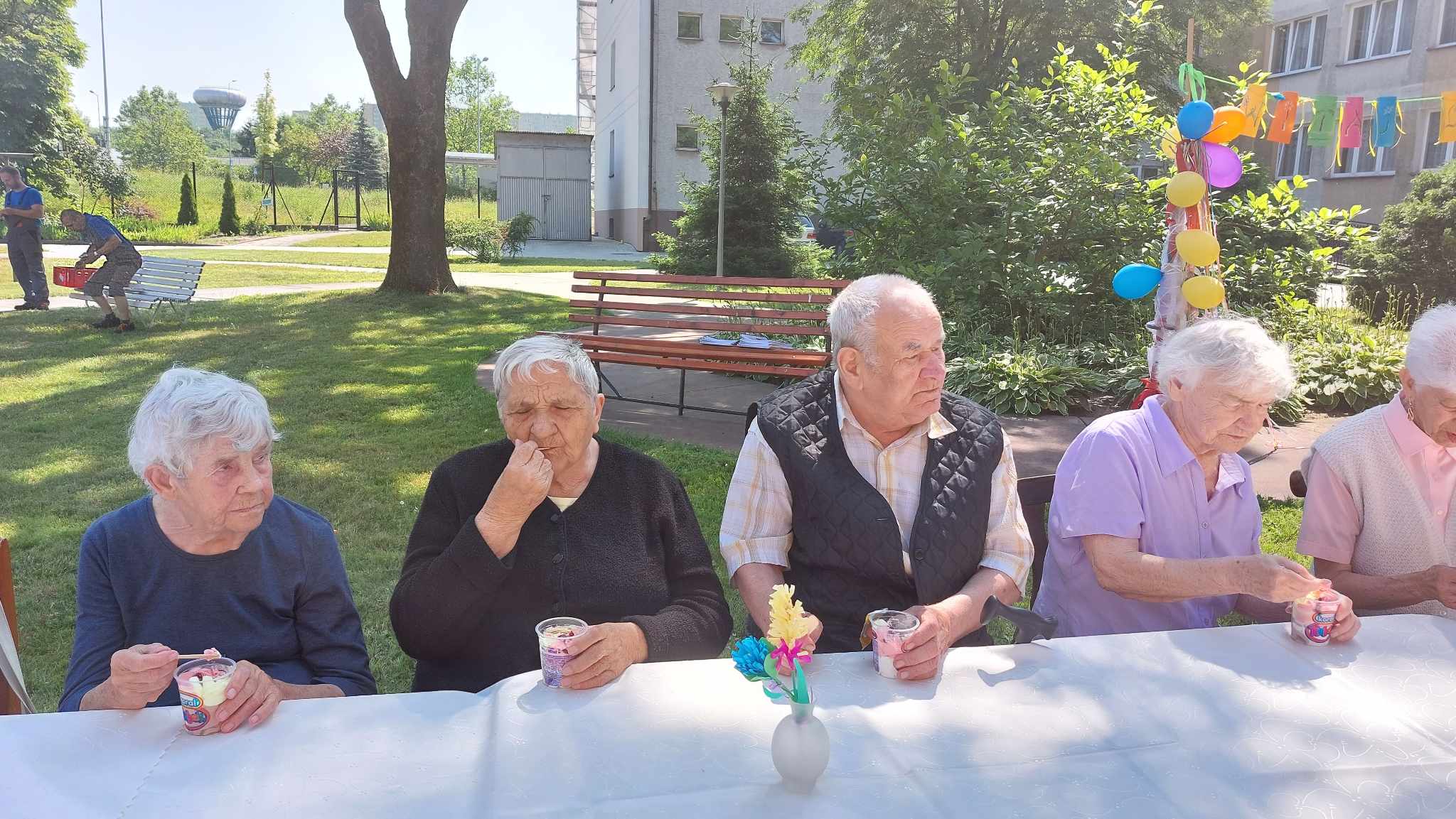 Cztery Seniorki i jeden Senior siedzą przy stole i jedzą lody