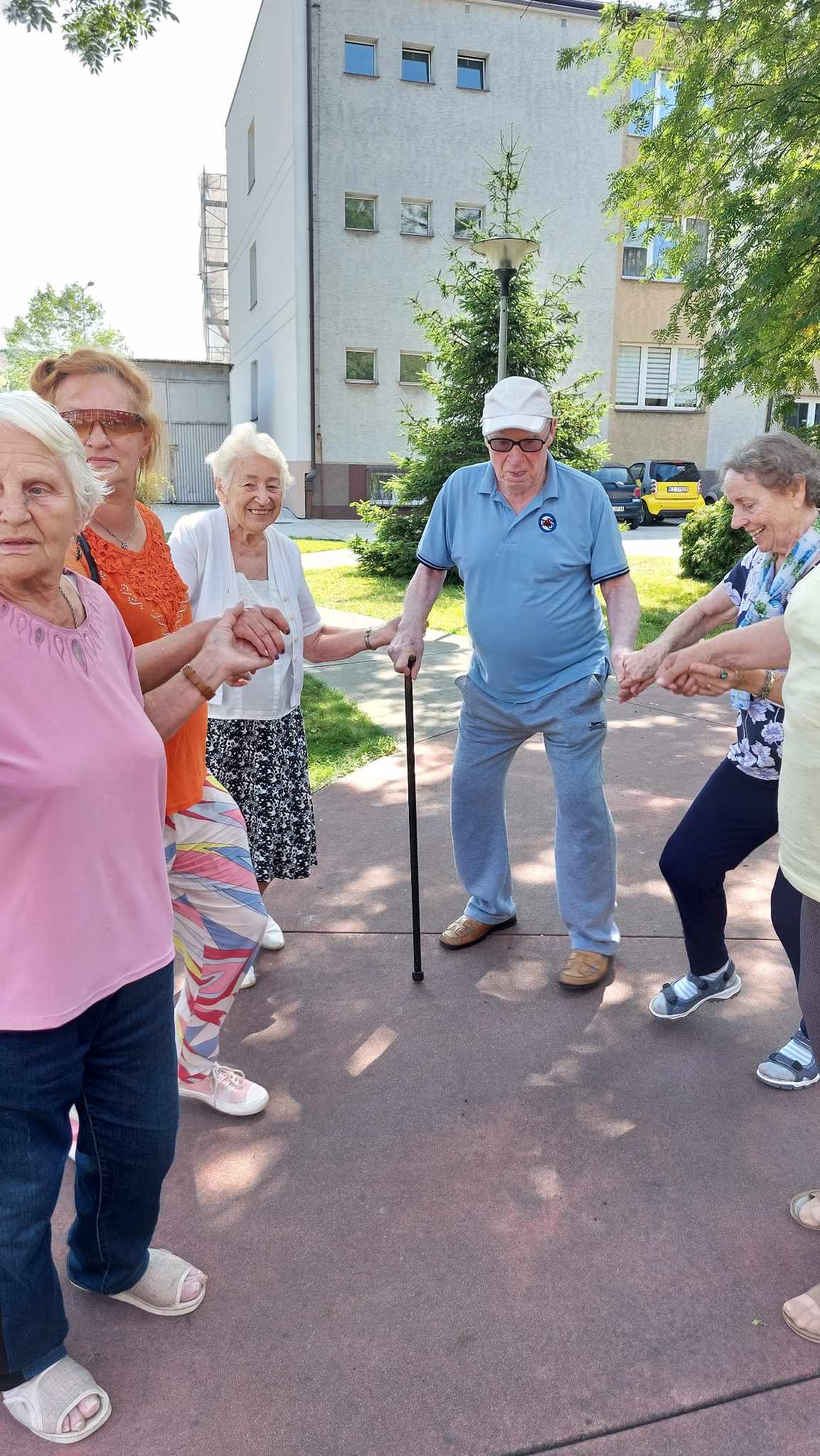 Seniorzy tańczą w kółku, trzymając się za ręce