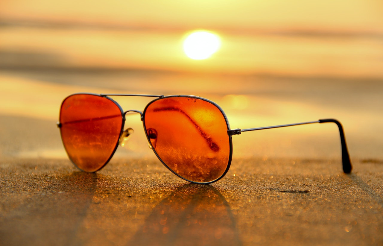 Okulary przeciwsłoneczne, leżące na piasku, w tle zachód słońca