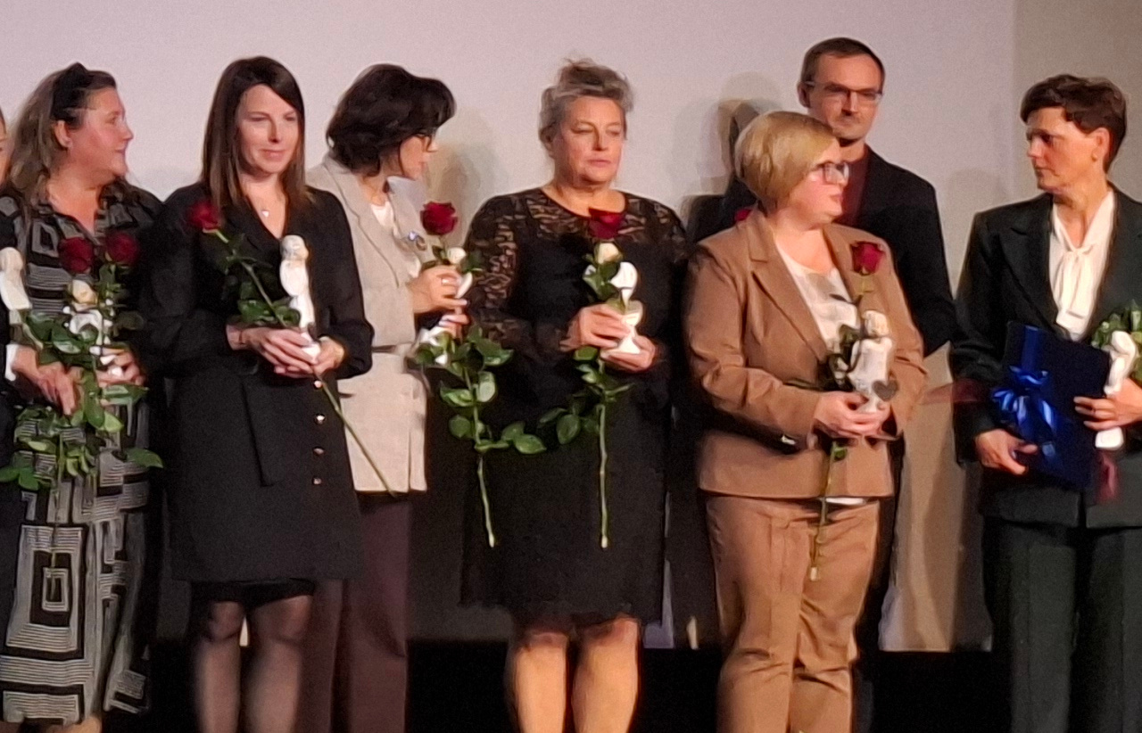 Zdjęcie zrobione na świetlicy Domu Seniorzy siedzą na krzesłach z tyłu,a z przodu na podłodze po turecku siedzą dzieci