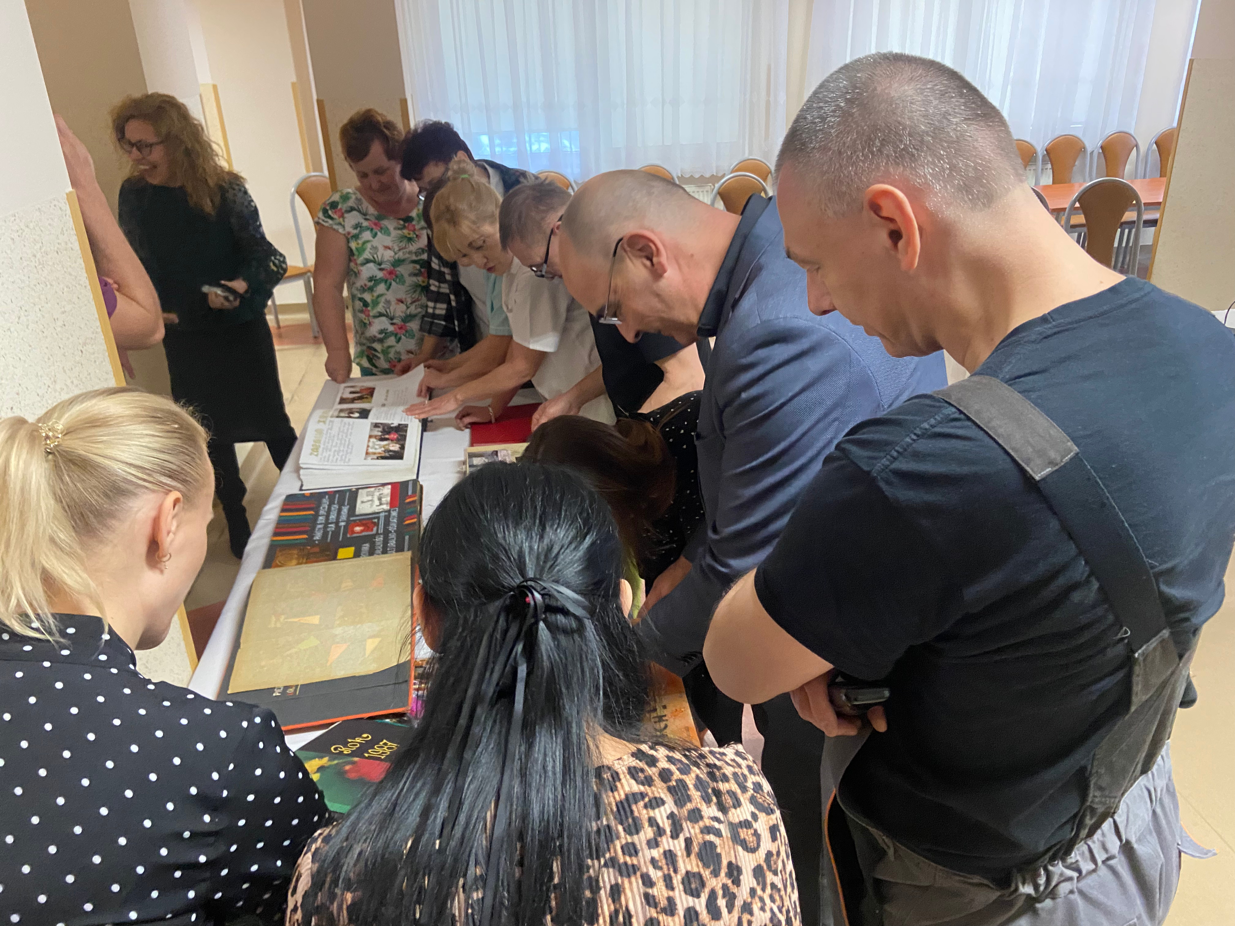 Pracownicy Domu stoją wokół stołu, na którym znajdują się kroniki Domu