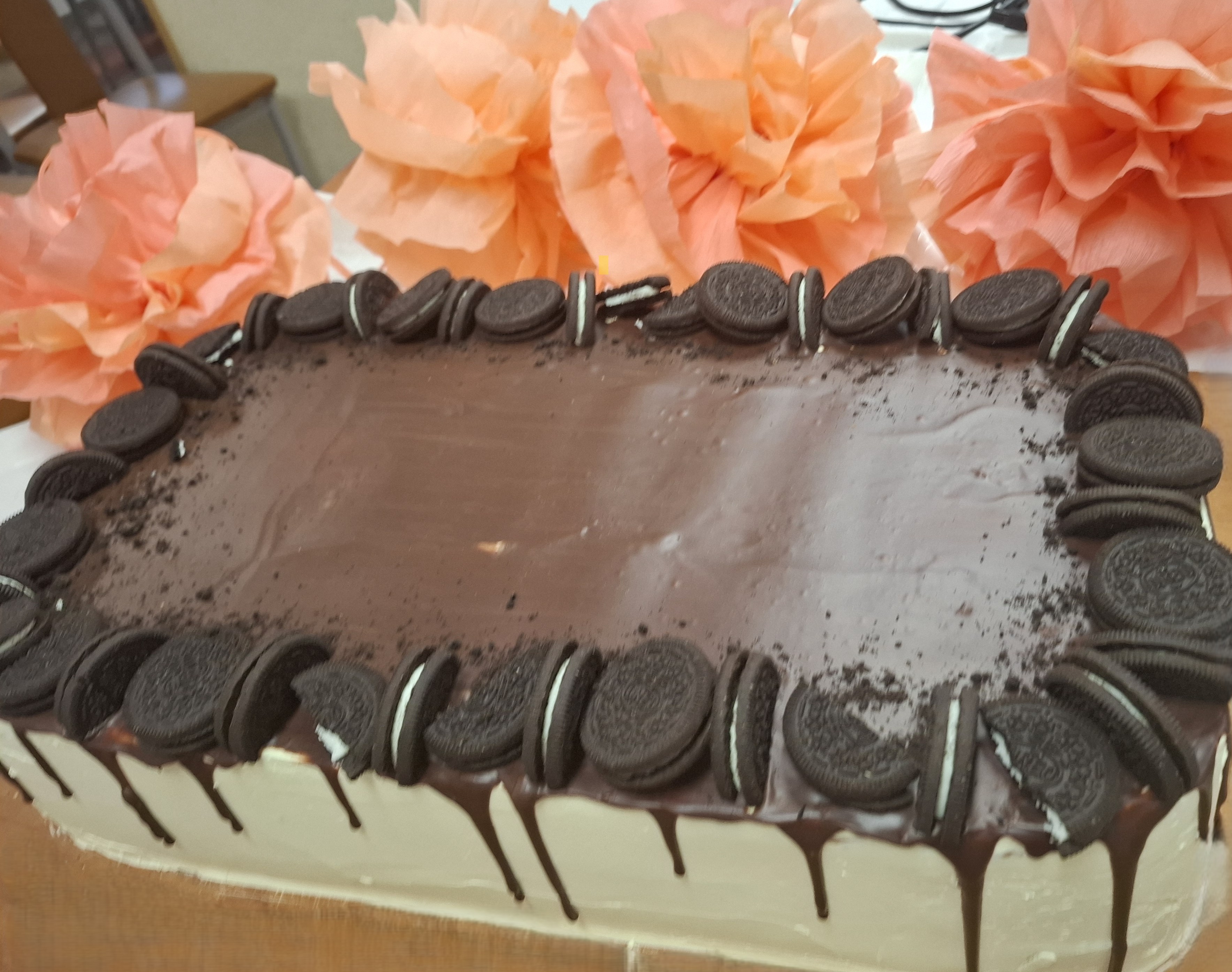 Zdjęcie tortu z ciemną polewą na górze dokoła ozdobiony ciasteczkami, boki tortu pokryte są białą masą