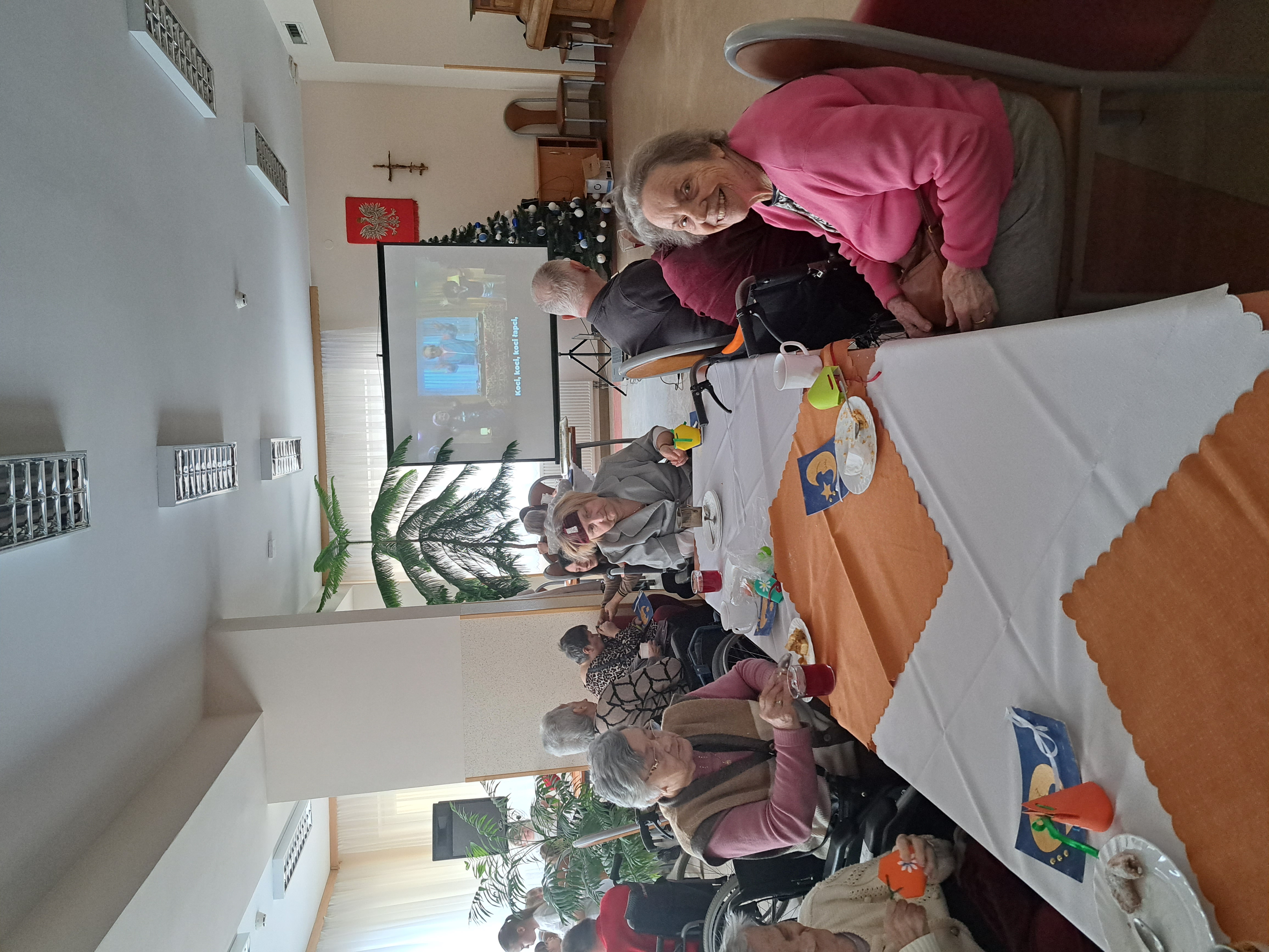 Seniorzy siedzą przy stole, jedzą ciasteczka i piją kawę