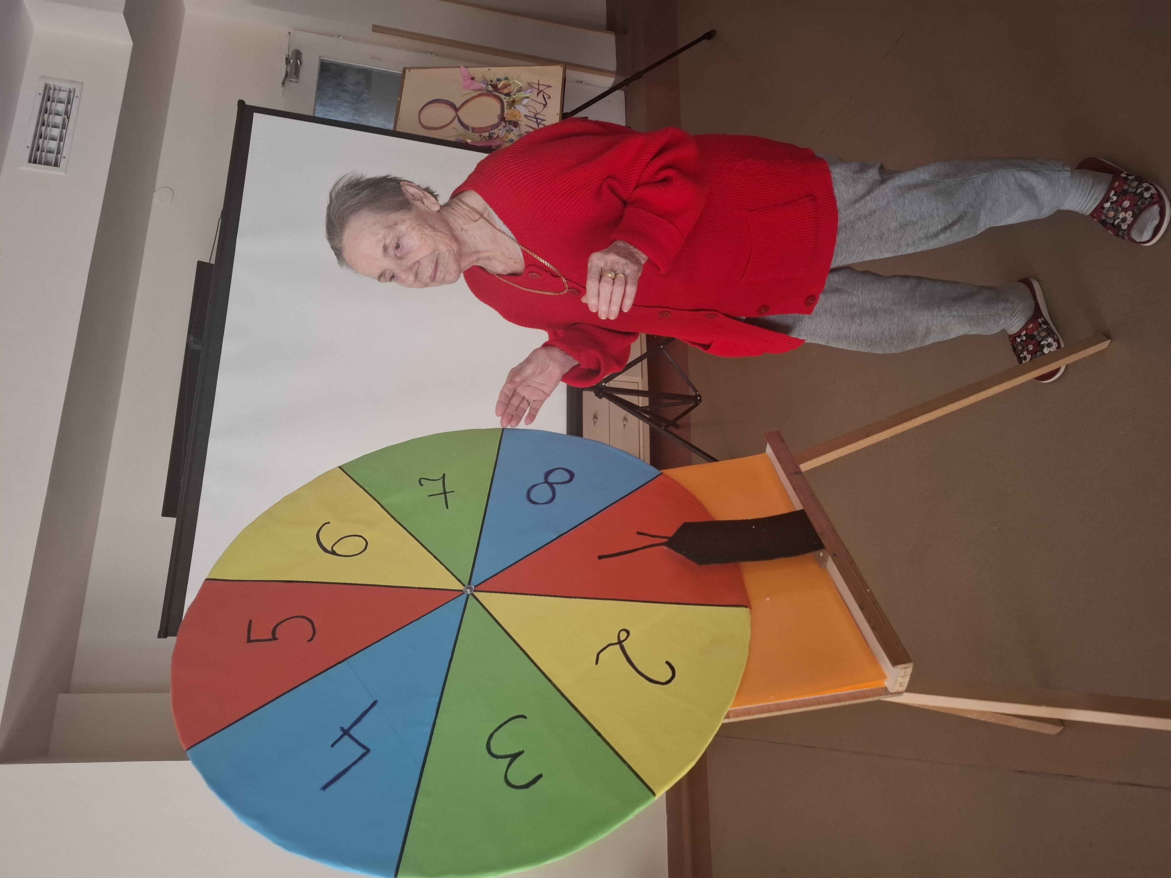 Seniorka stoi przy ręcznie zrobionym kolorowym kole fortuny