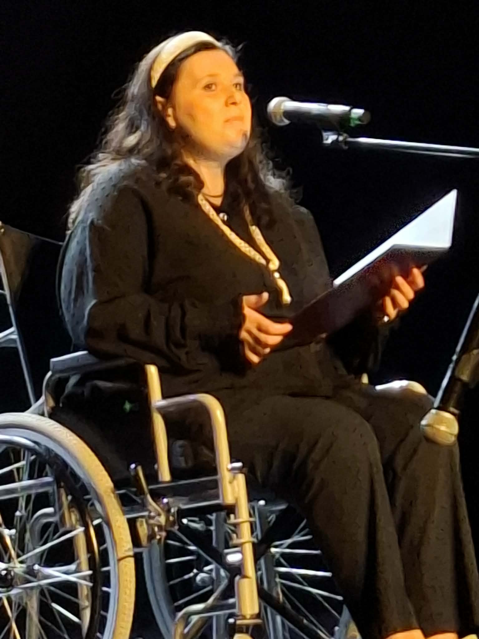 Kobieta siedząca na wózku inwalidzkim mówi do mikrofonu