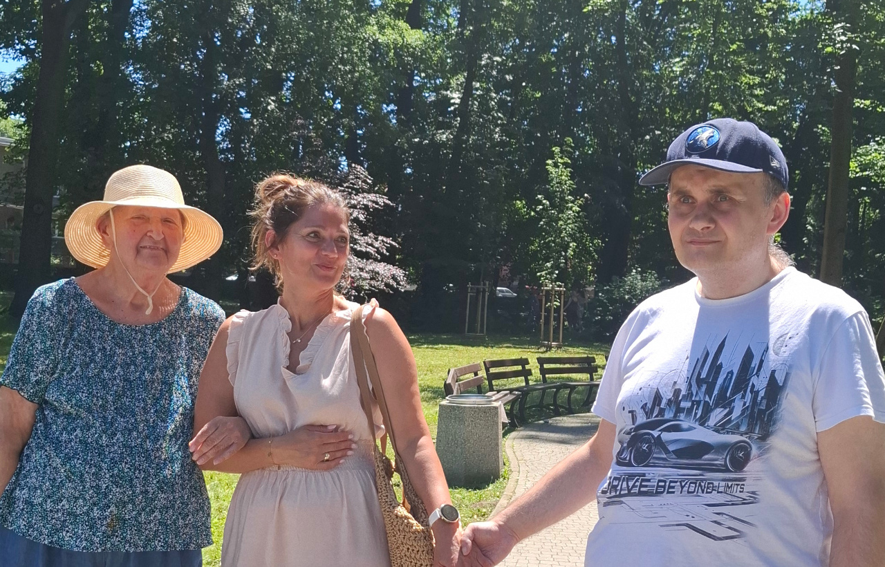 Zdjęcie ogrodu domu, w oddali widać rozłożone stoły, przy których siedzą Seniorzy