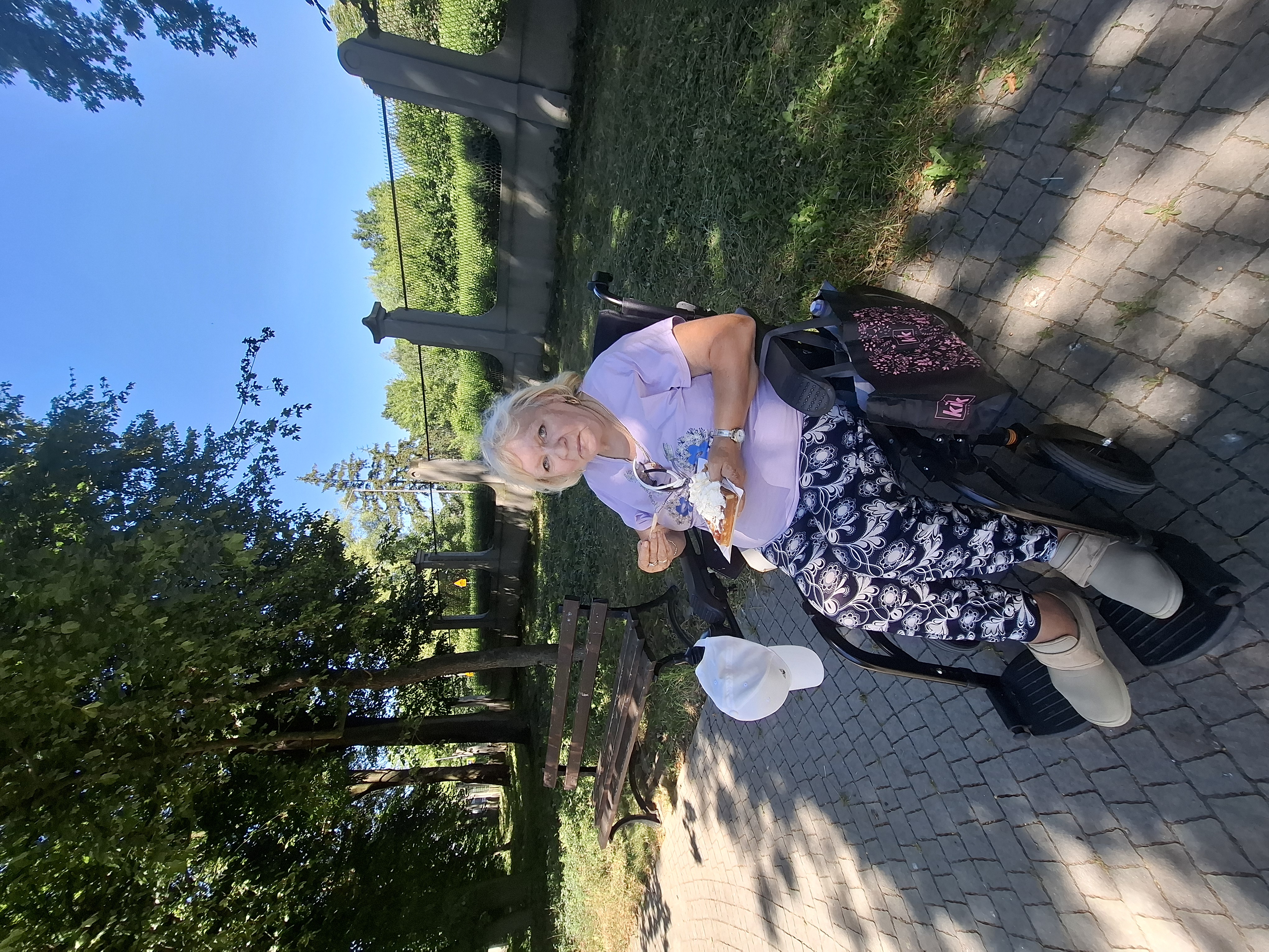 Seniorka siedząca na wózku inwalidzkim, pozuje do zdjęcia. W ręce trzyma gofra