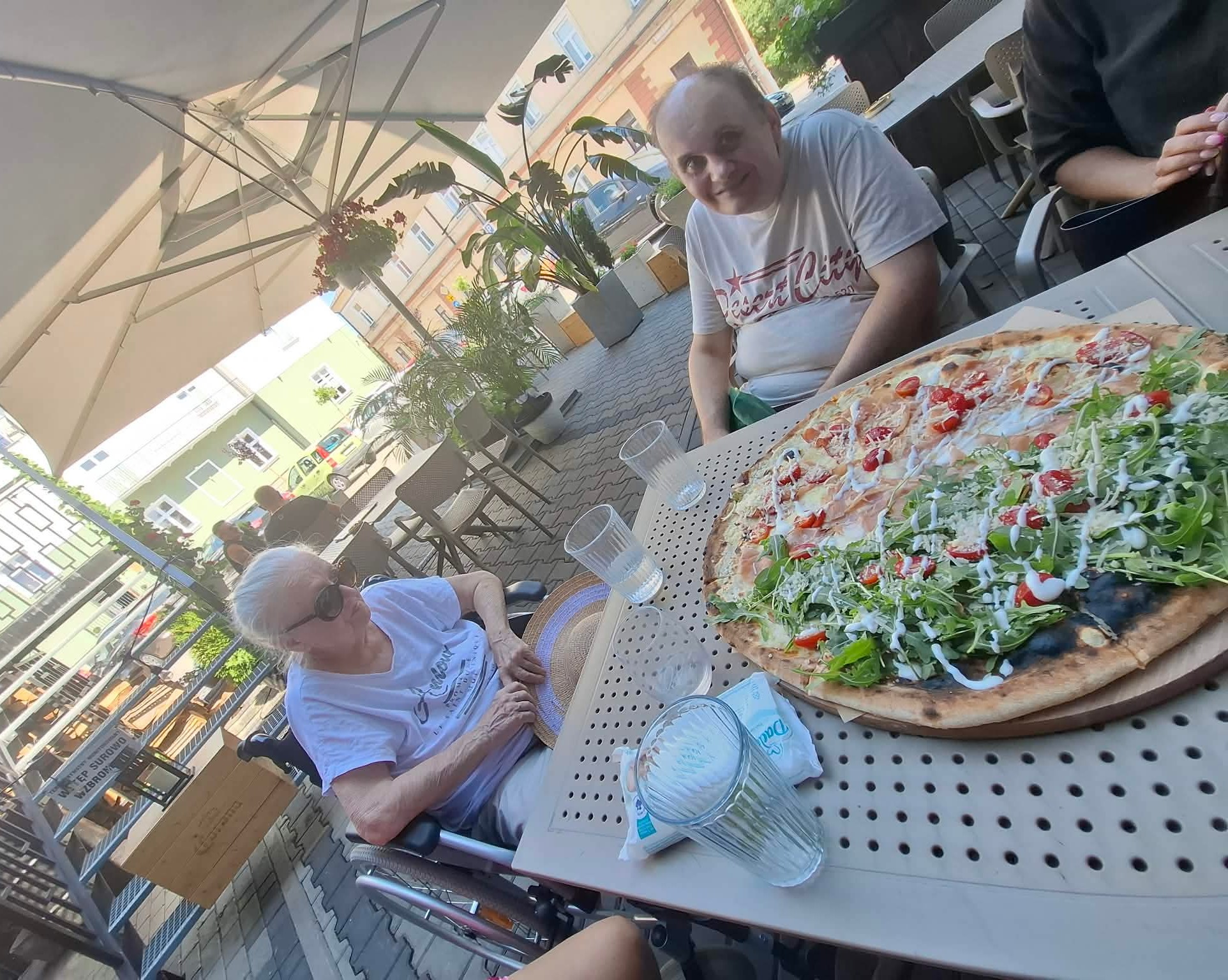 Seniorka i Senior siedzą przy stoliku, na którym stoi pizza