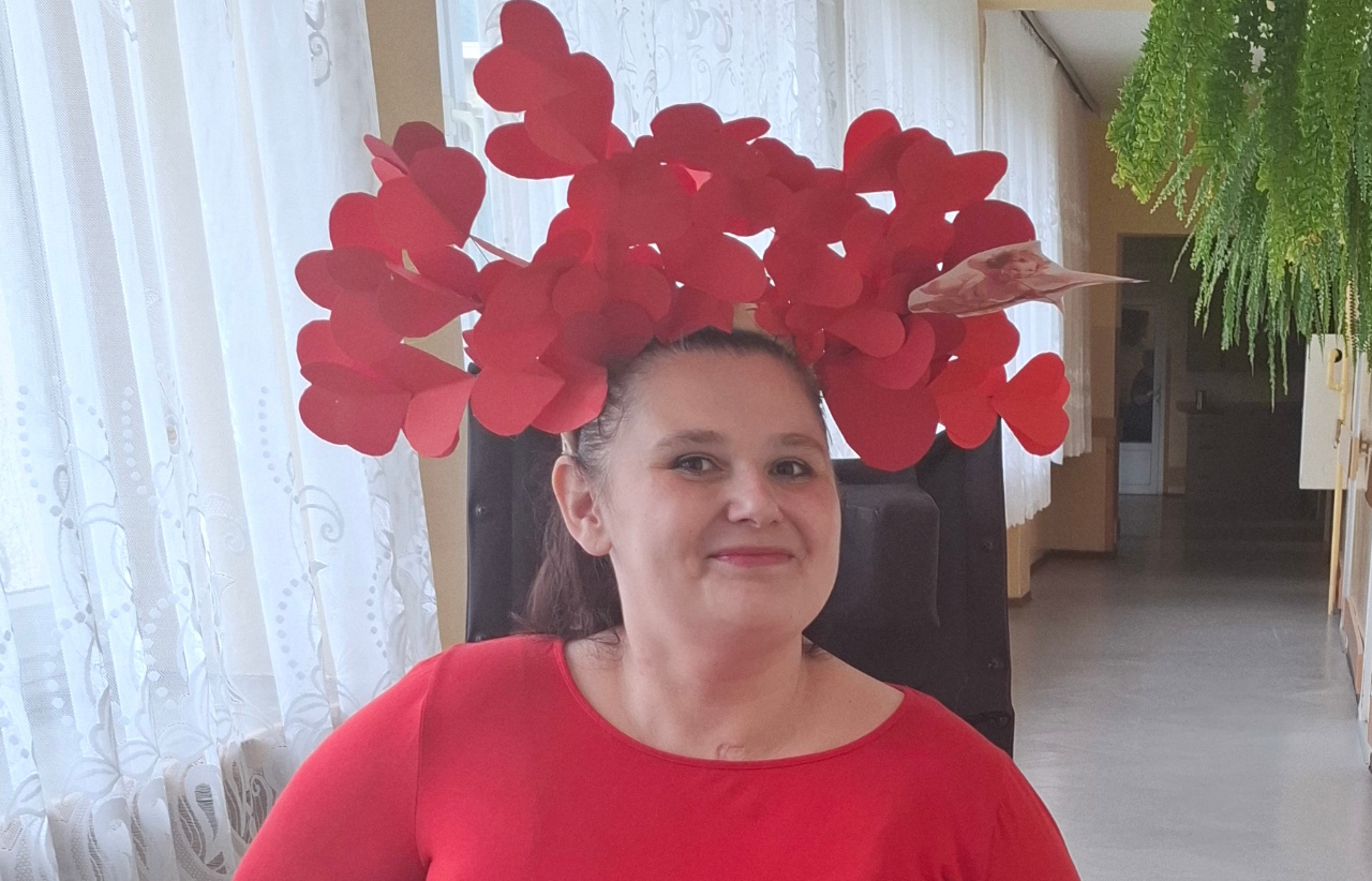 Zdjęcie portretowe kobiety ubranej w czerwone ubrania, na głowie ma ozdobę zrobioną z papierowych serduszek